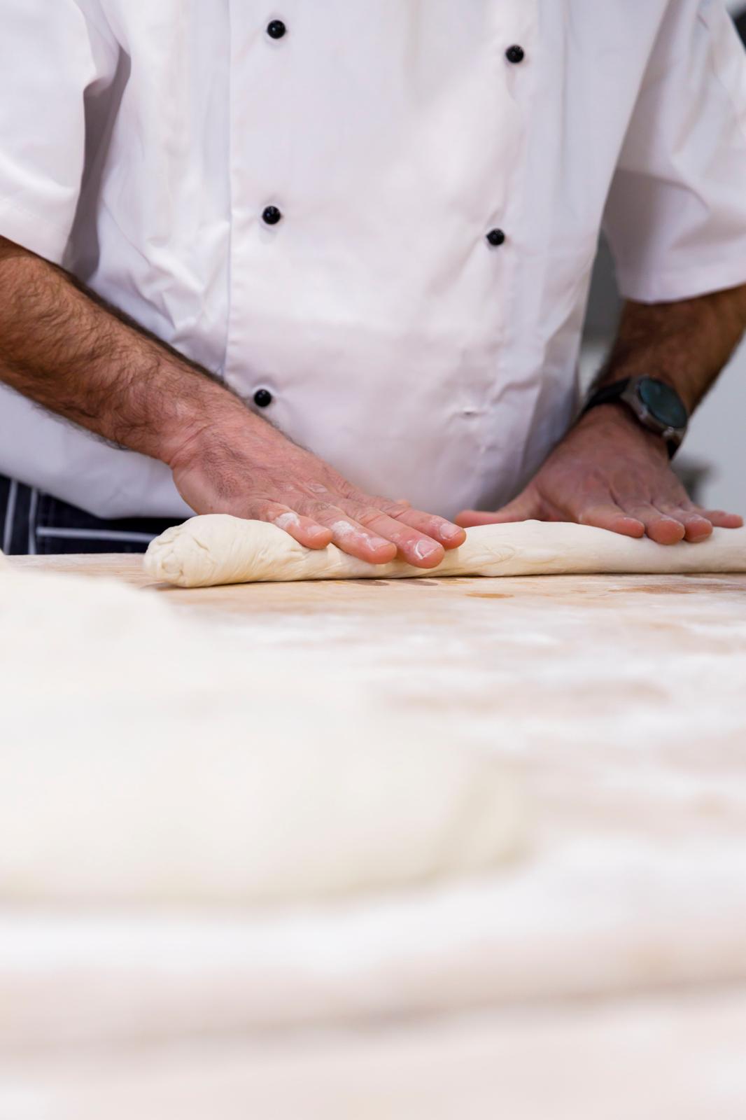 Hands rolling shaped dough on a floured bench
