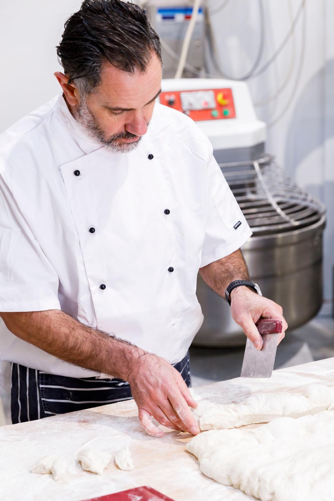 Head baker dividing dough beside the spiral mixer